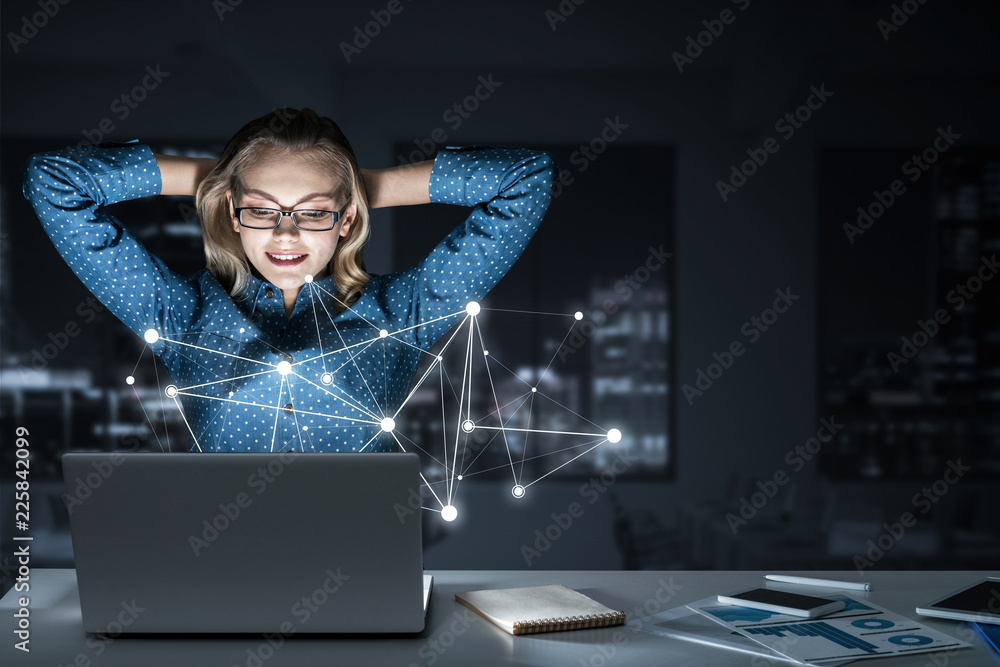 Attractive blonde wearing glasses in dark office using laptop. M