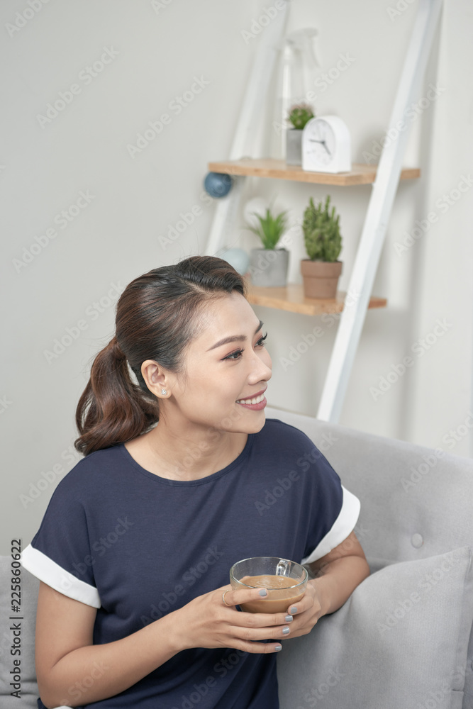 Portrait of a pensive woman holding a cup of coffee relaxing sitting on a couch in the living room a