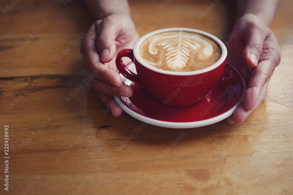 Hot coffee latte cappuccino in red cup and saucer with beautiful latte art milk foam on baristas ha