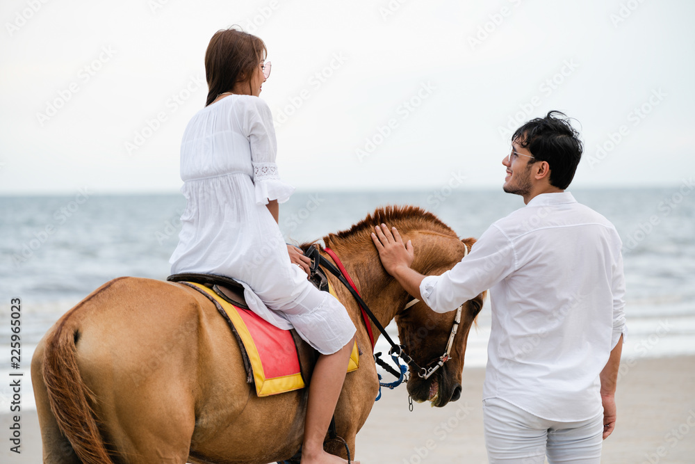 一对年轻夫妇在热带海滩上骑马。