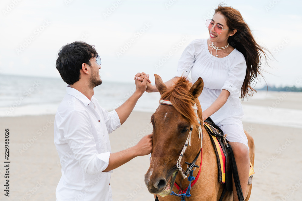 一对年轻夫妇在热带海滩上骑马。