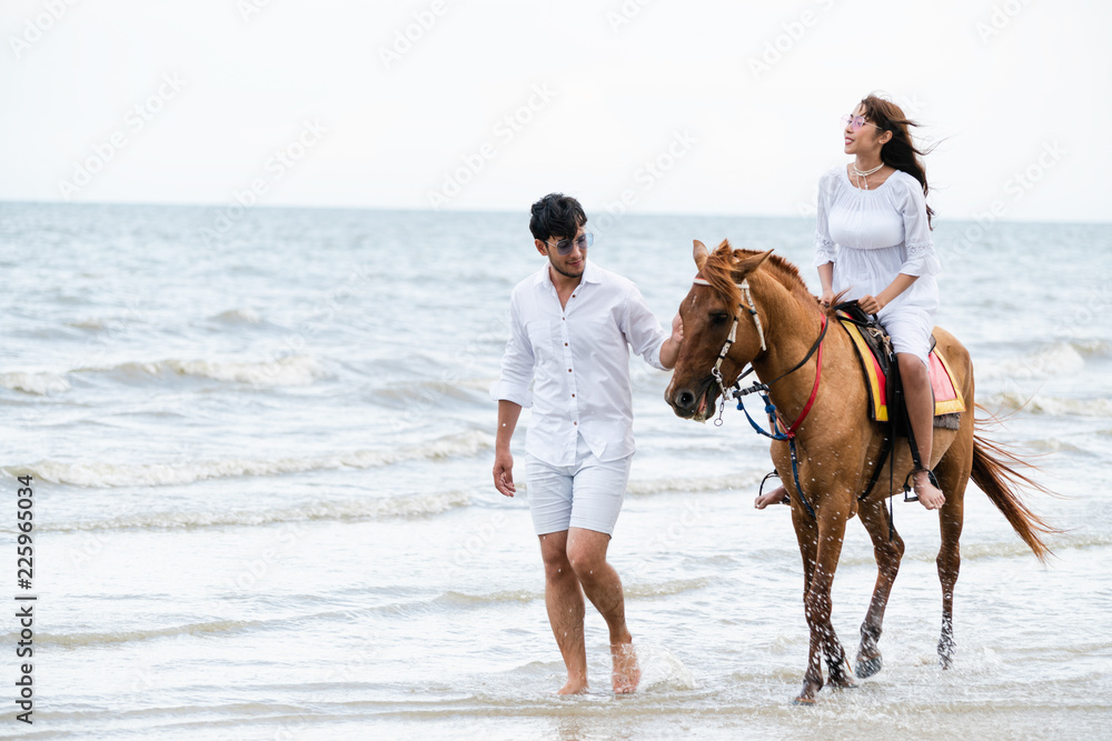 一对年轻夫妇在热带海滩上骑马。