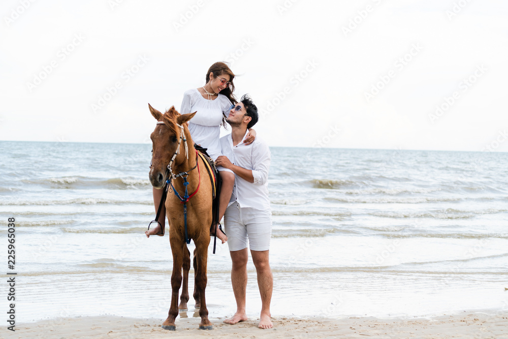 一对年轻夫妇在热带海滩上骑马。