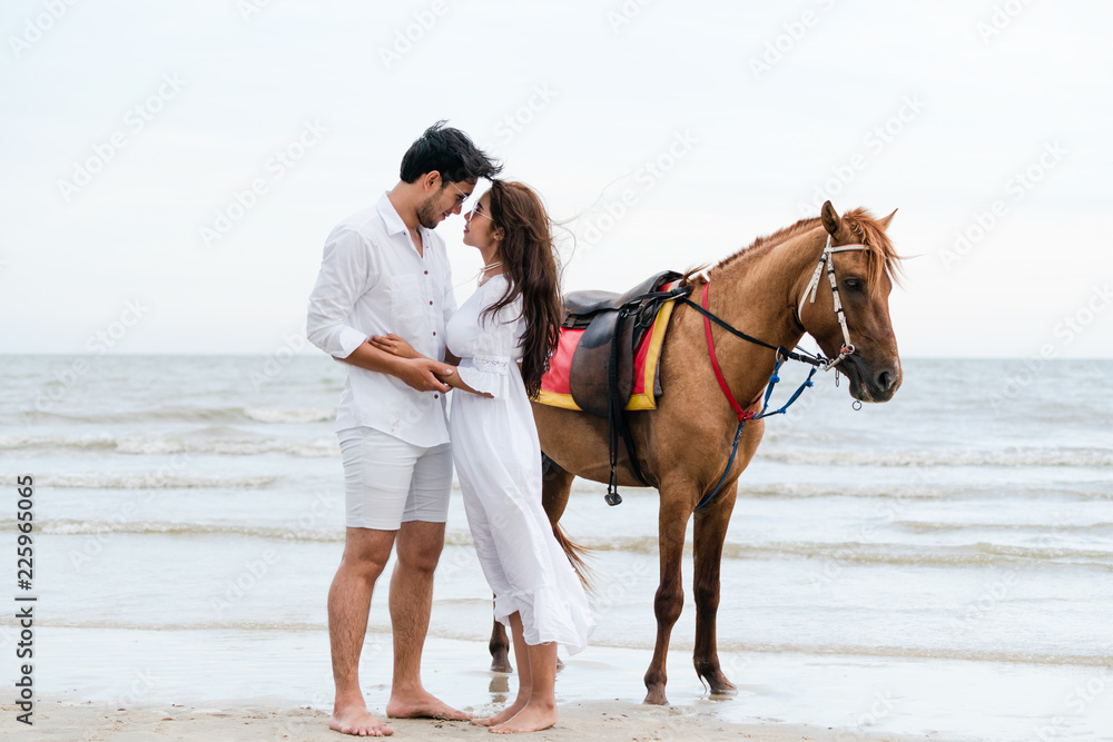 一对年轻夫妇在热带海滩上骑马。