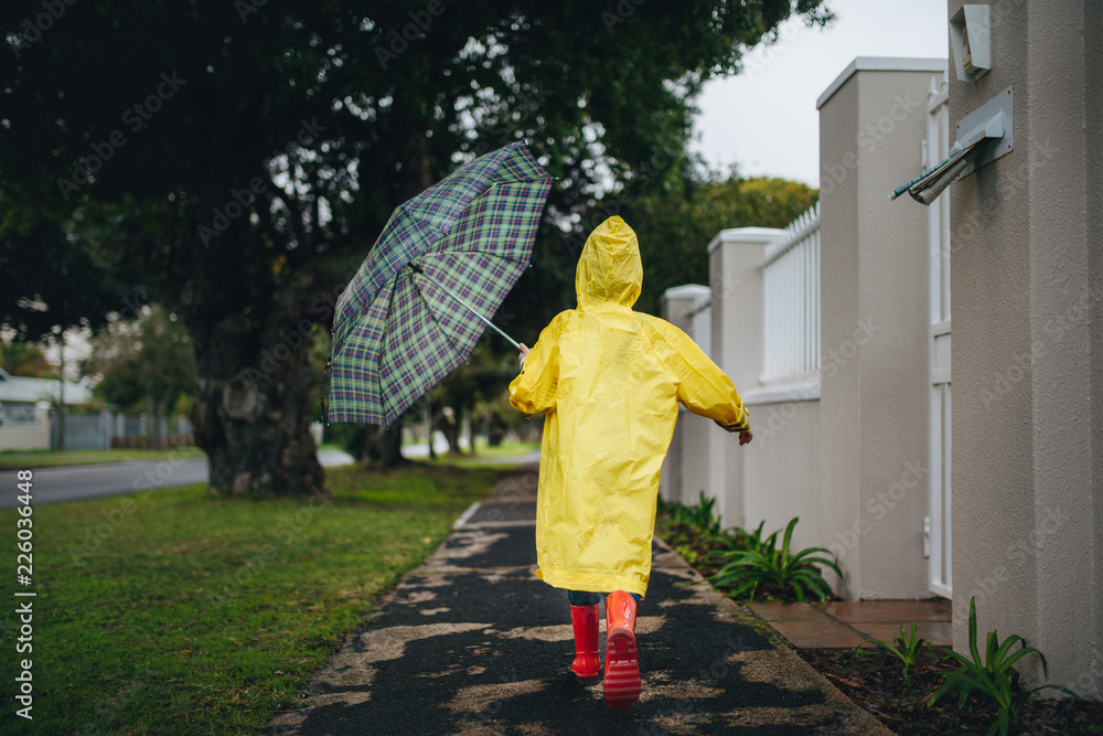 穿着防水服、打着雨伞的女孩在户外跑步