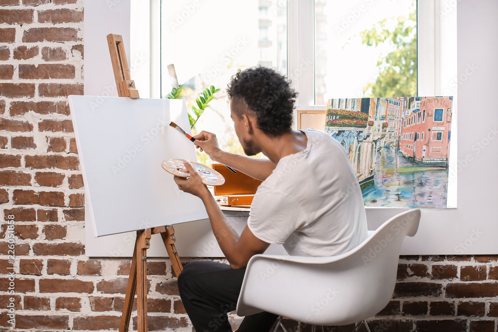 Young African-American artist painting picture in workshop