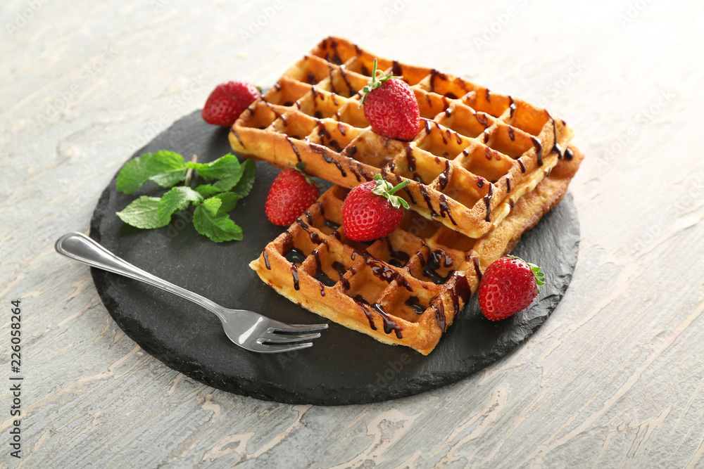 Delicious waffles with strawberries and chocolate sauce on slate plate