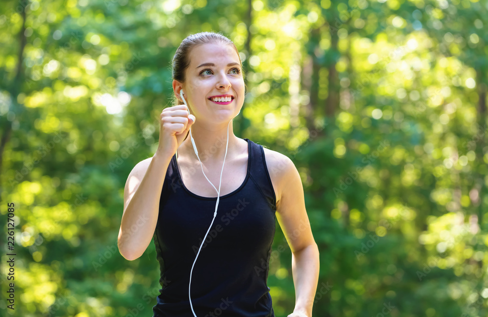 Athletic young woman jogging on a bright summer day in the forest