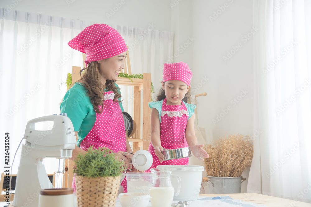 Beautiful asian mother and daughter wearing pink apron making cake in the kitchen.