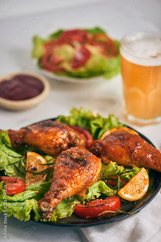 Grilled chicken legs roasted on the grill on dark plate with tomato sauce in a bowl and lettuce leav