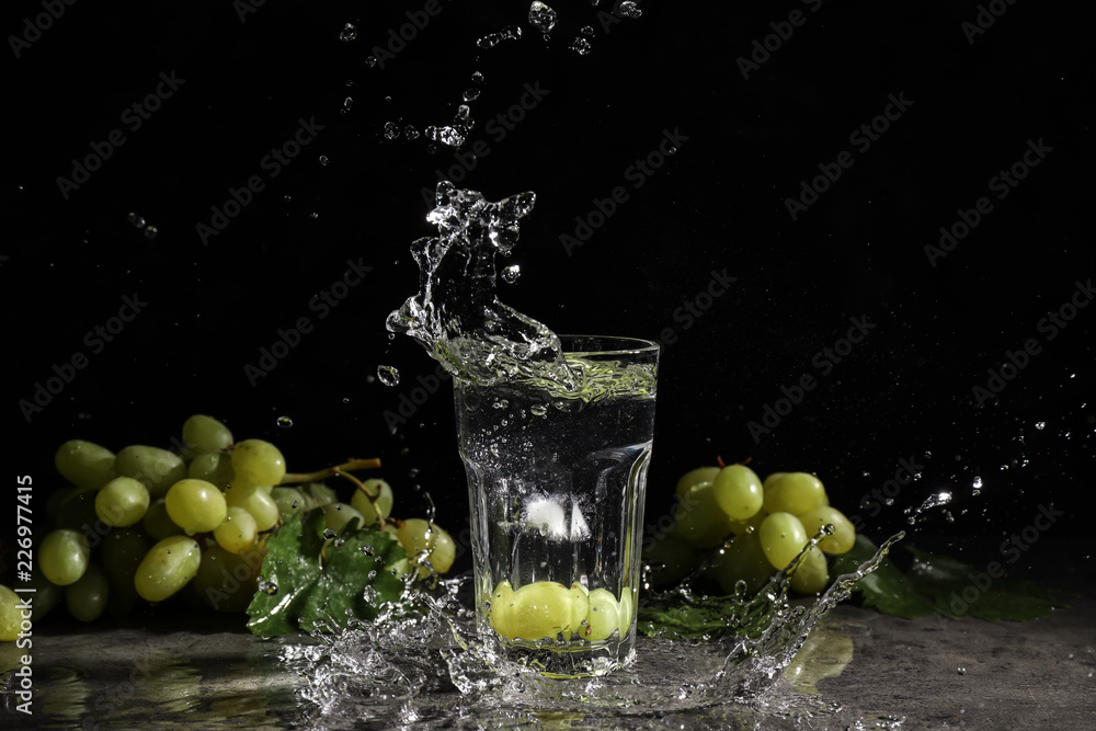 Ripe juicy grapes and glass of water with splashes on dark background