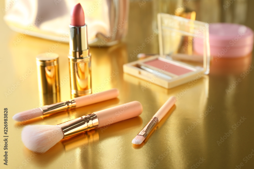 Makeup brushes and pink lipstick on golden table