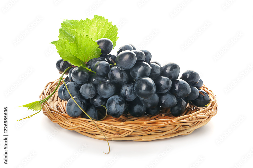 Wicker plate with ripe sweet grapes on white background