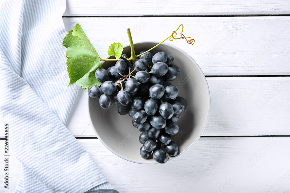 Plate with ripe sweet grapes on white wooden background