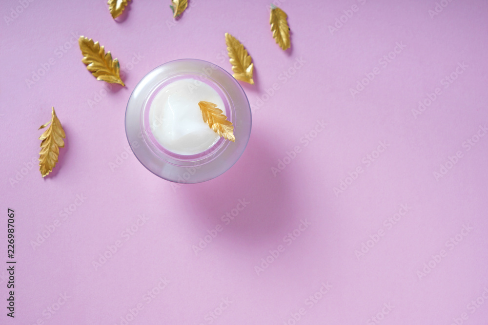 Jar with body cream and golden leaves on color background