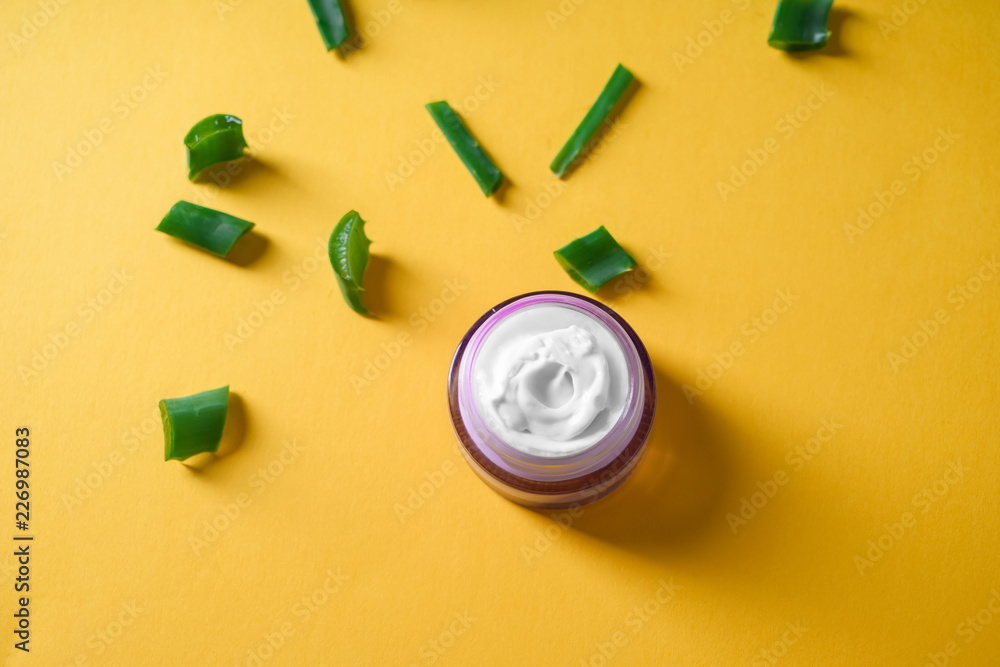 Jar with body cream and cut aloe vera on color background