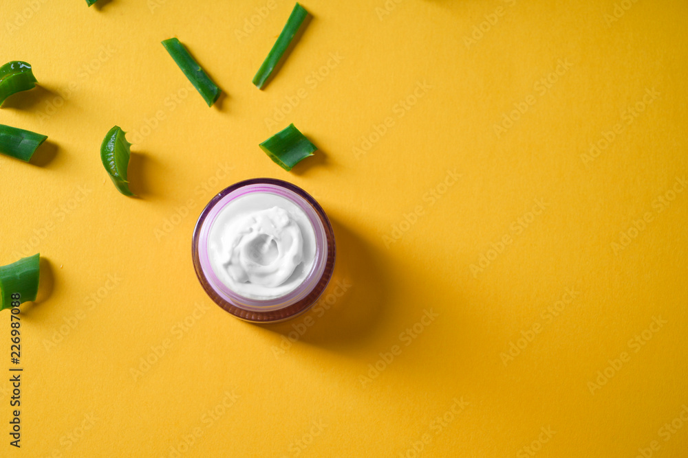 Jar with body cream and cut aloe vera on color background