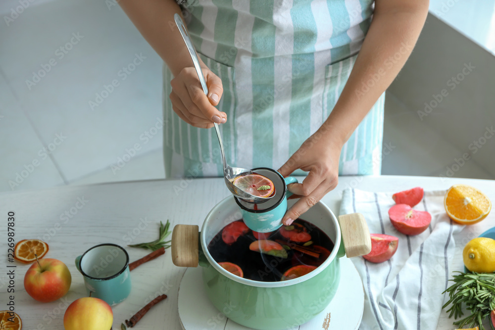 女人把热腾腾的热葡萄酒从勺子里倒进桌子上的杯子里