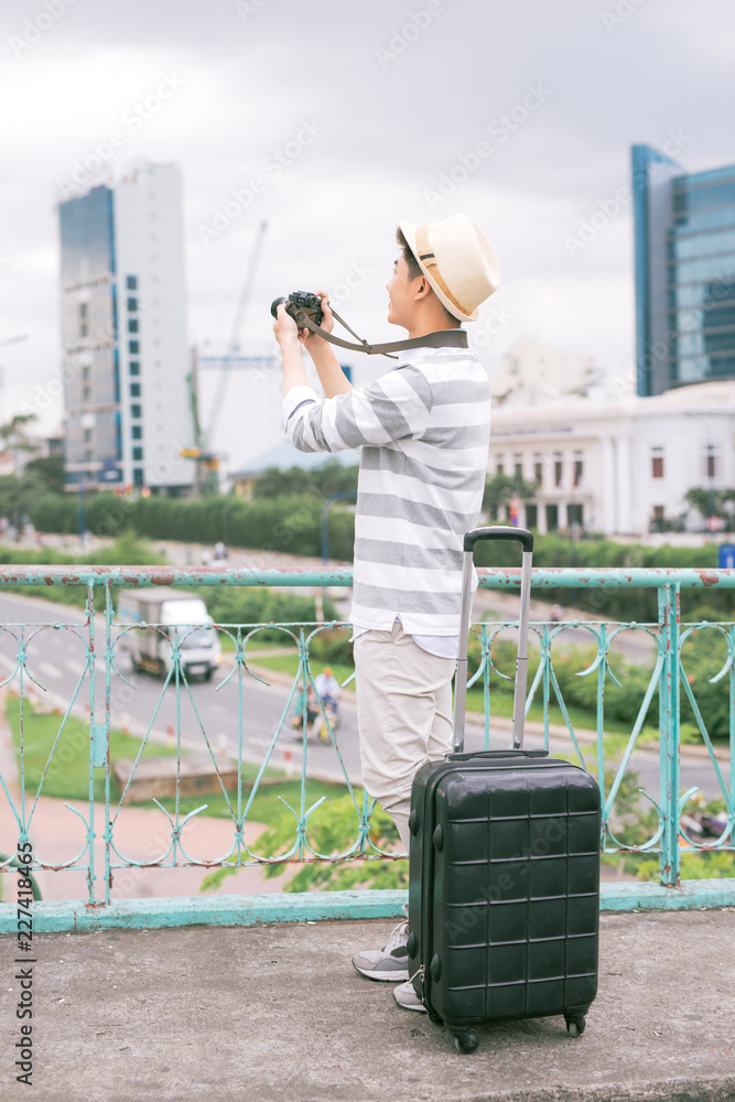 年轻时尚的亚洲男子带着行李箱和相机旅行。