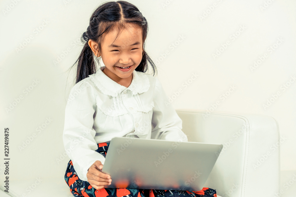 Little happy kid using laptop computer sitting on white sofa. Childhood lifestyle.