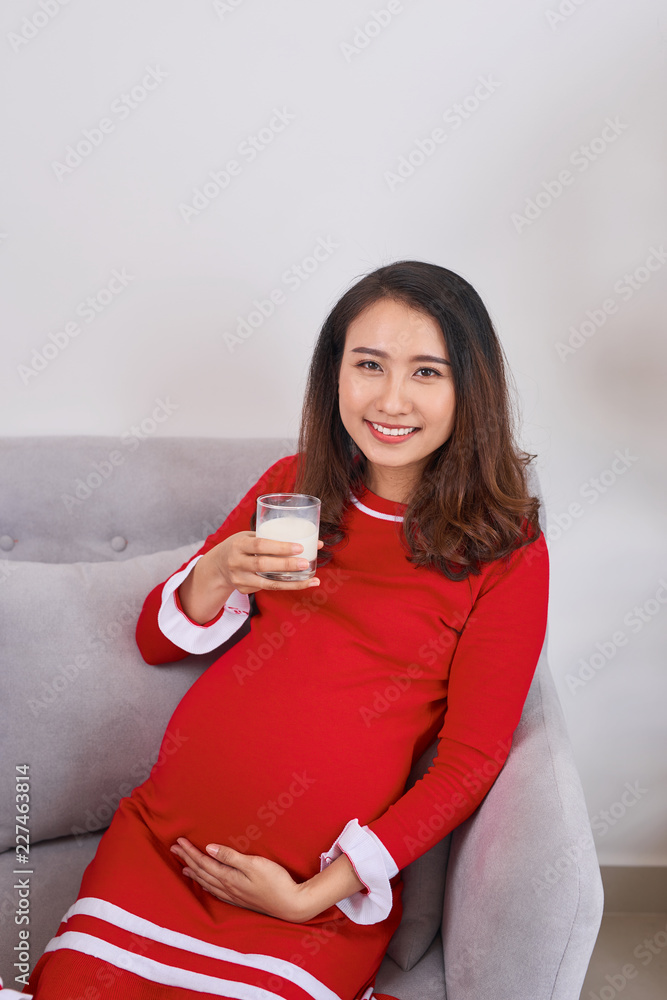 Beautiful pregnant woman is sitting on sofa and looking at the camera.