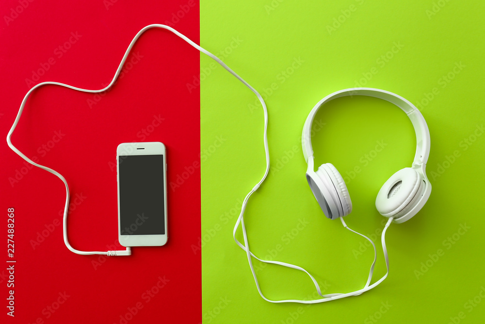 Mobile phone with headphones on color background