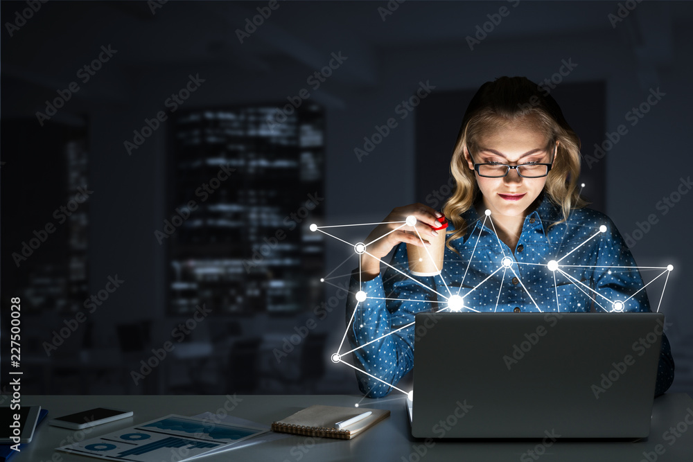 Attractive blonde wearing glasses in dark office using laptop. Mixed media