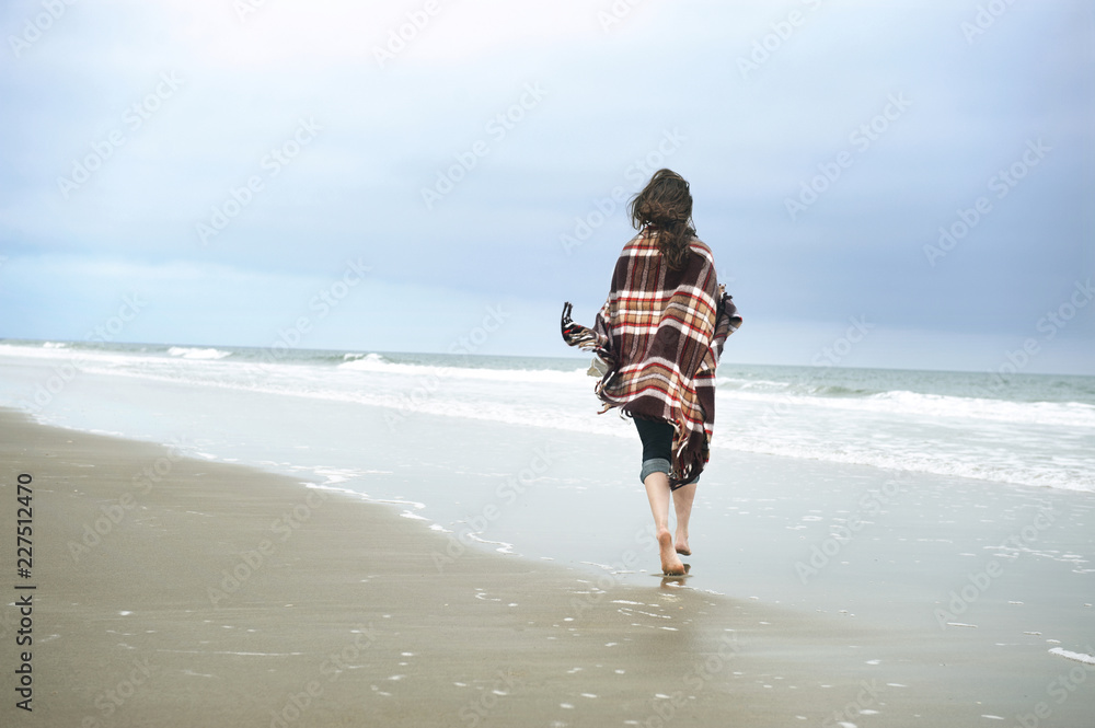 裹着毯子走在海边的女人的后视图