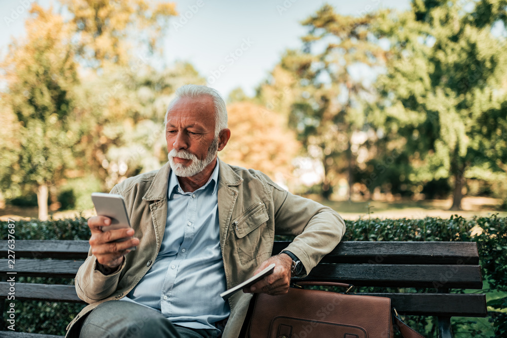 Senior man sitting on the bench and using smartphone.