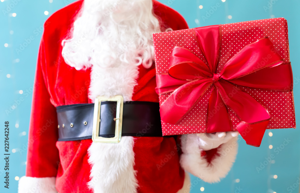 Santa holding a Christmas gift on a shiny light blue background