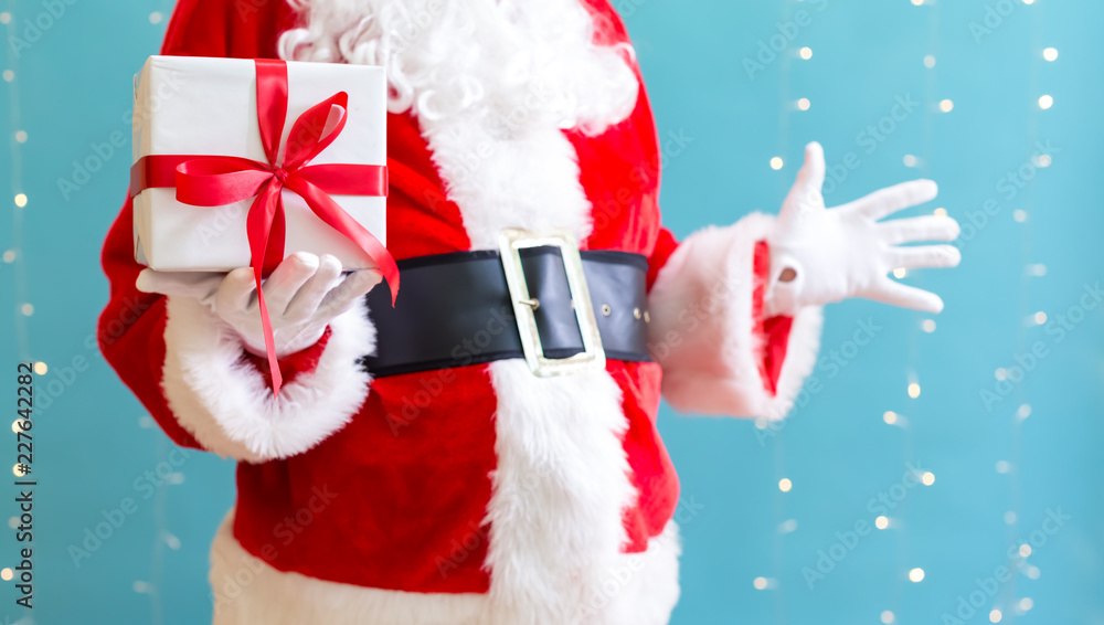 Santa holding a Christmas gift on a shiny light blue background