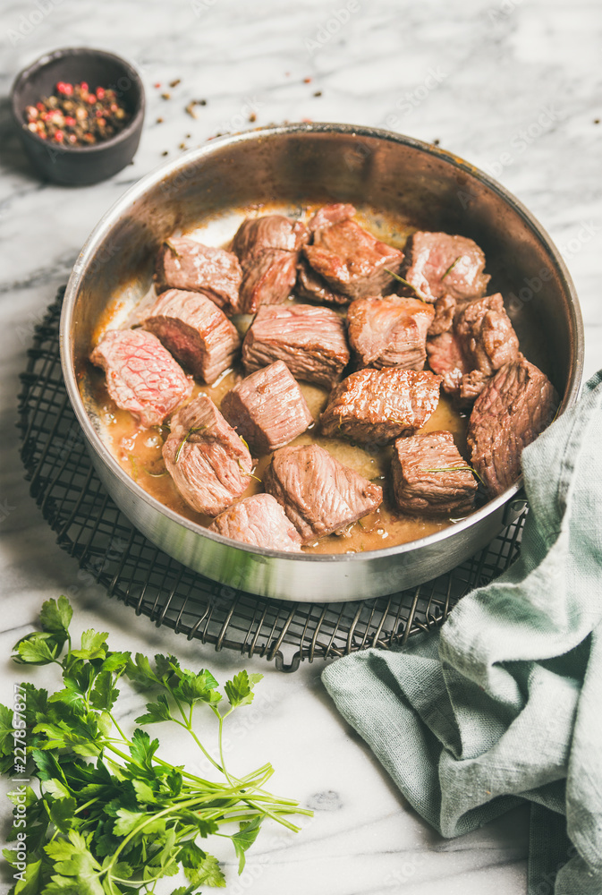 肉类晚餐。在白色大理石台面上的烹饪锅中用新鲜欧芹炖牛肉