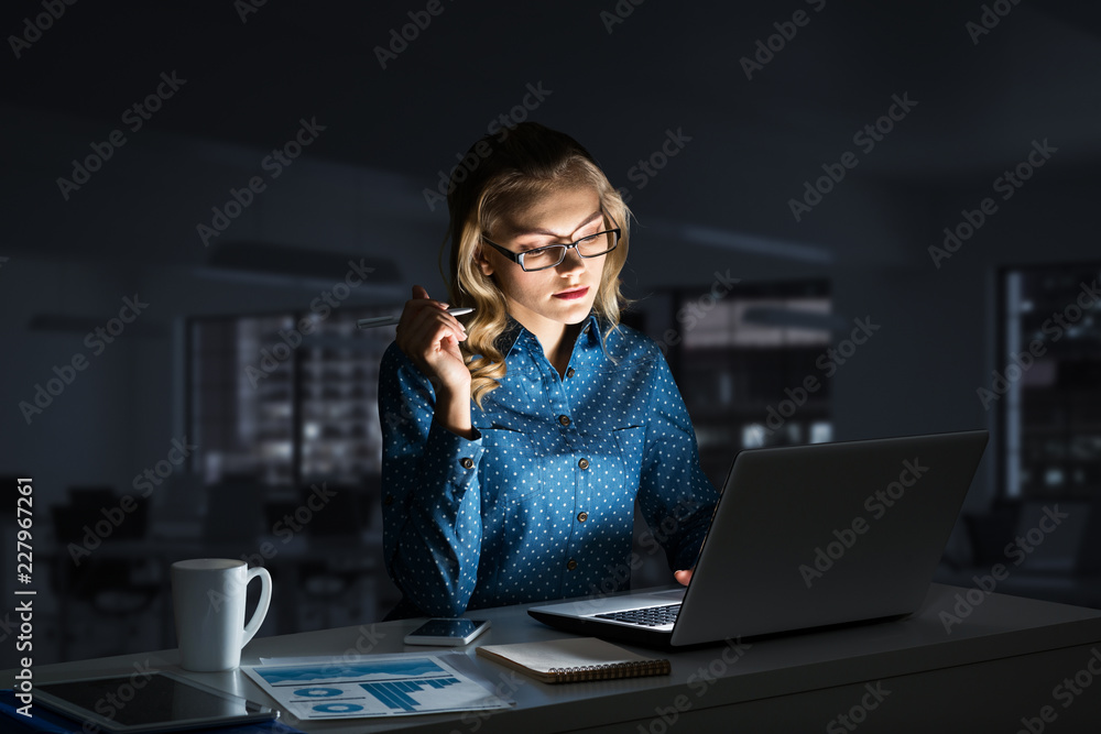 Attractive blonde working on laptop in dark office. Mixed media