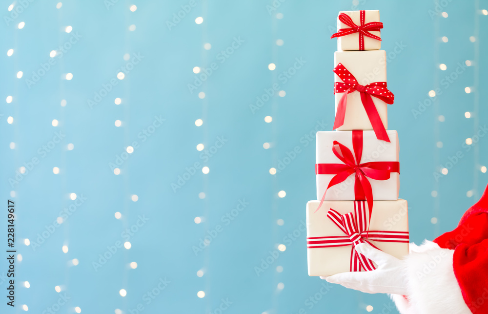 Santa holding Christmas gift boxes on a shiny light blue background