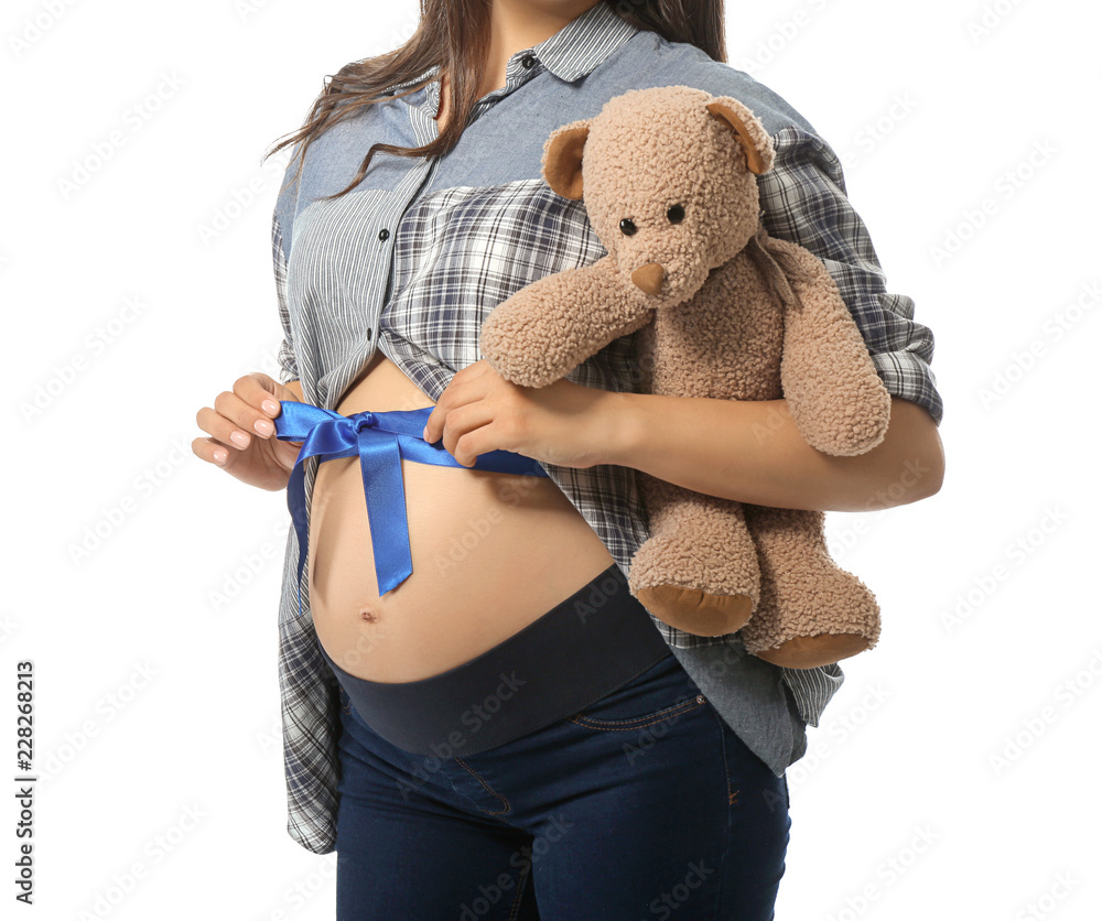 Beautiful pregnant woman with toy bear and blue ribbon on her belly against white background