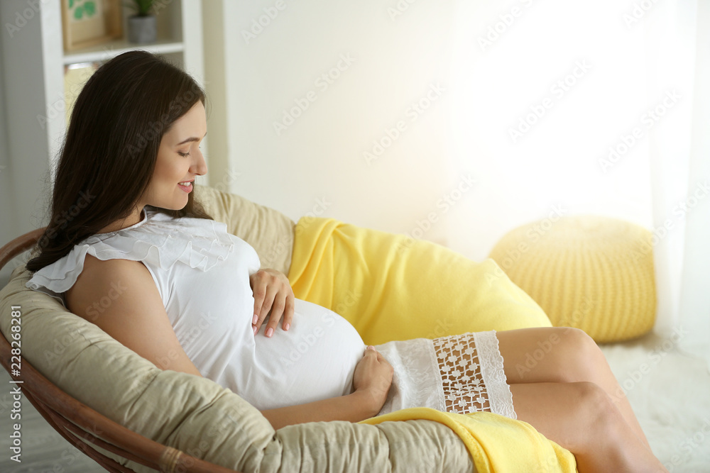 Beautiful pregnant woman sitting in armchair at home