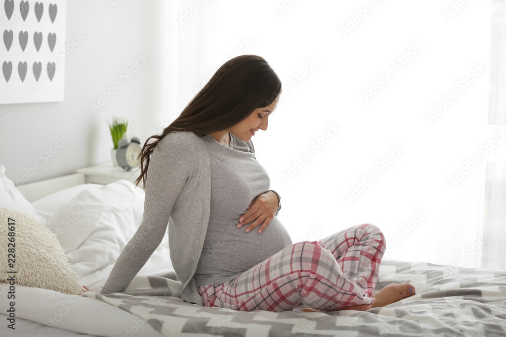 Beautiful pregnant woman sitting on bed at home