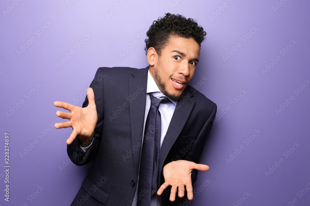 Portrait of emotional African-American businessman on color background