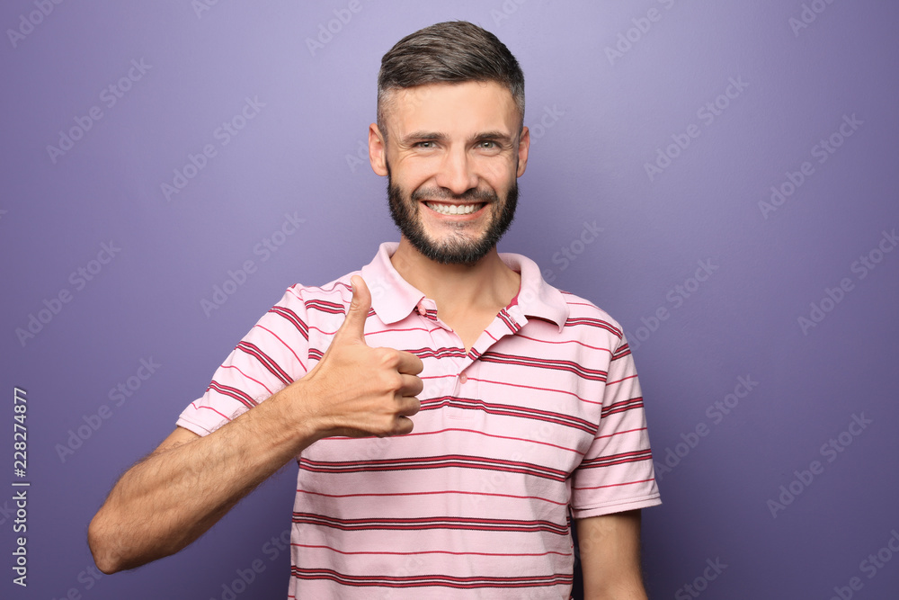 Happy man showing thumb-up gesture on color background