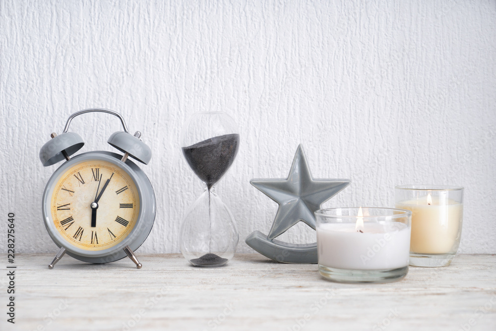 Beautiful burning candles with alarm clock and hourglass on light wooden table