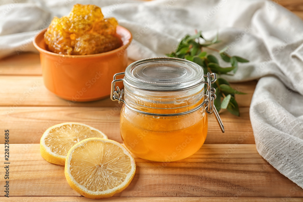 Jar with honey and lemon slices on wooden table