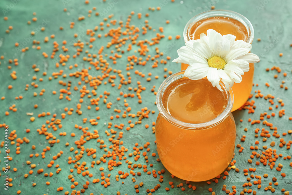 Jars of honey and flower on color background