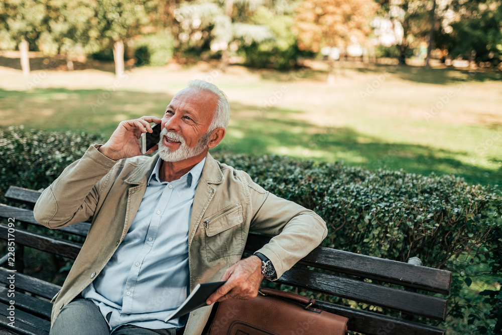 Older man talking on the mobile phone while sitting in the park.