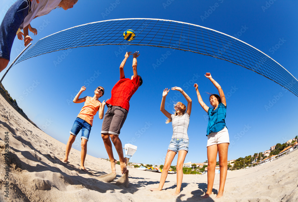 Active boys and girls playing volleyball on beach