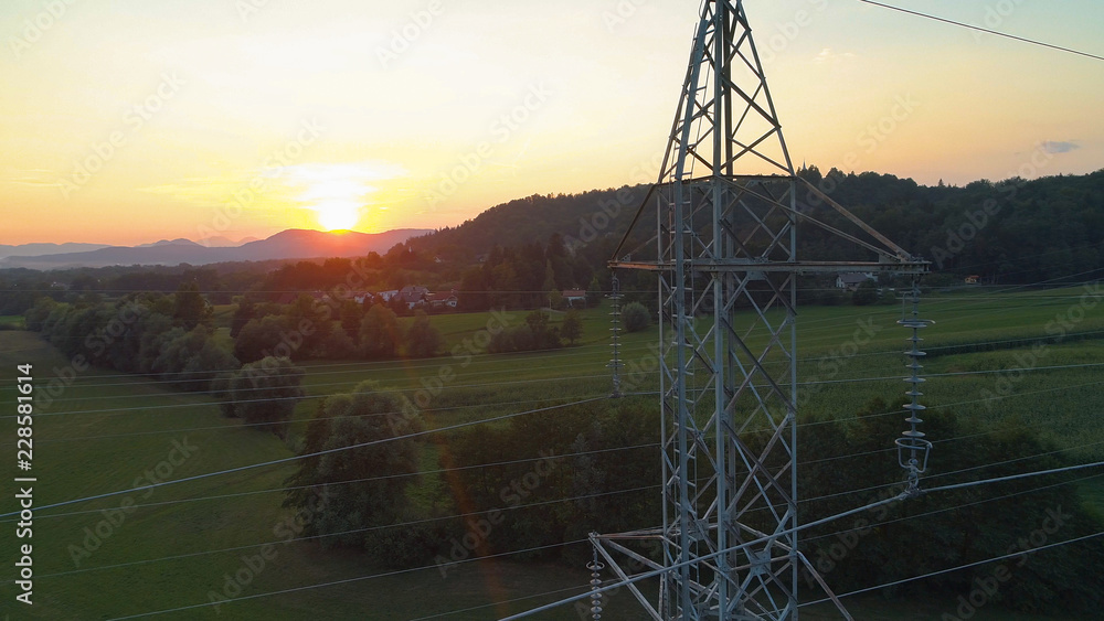 AERIAL: Golden evening sun shines on the metal power tower in the countryside.