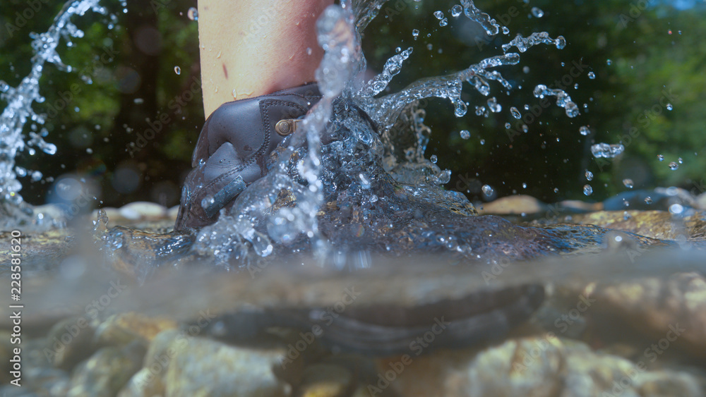 HALF UNDERWATER: Unknown female hiker splashing water by stepping into the river