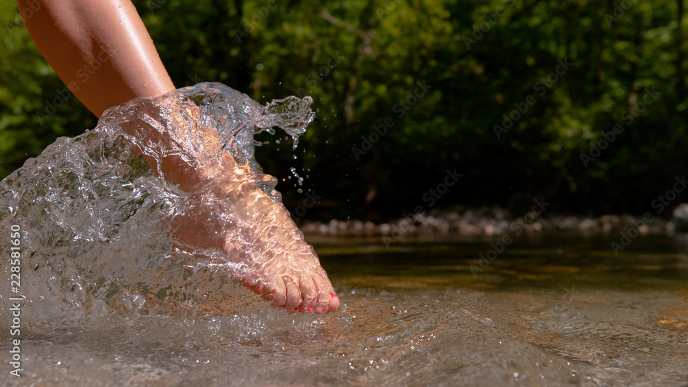 CLOSE UP: Barefoot girl with painted toenails kicking the calm river water.