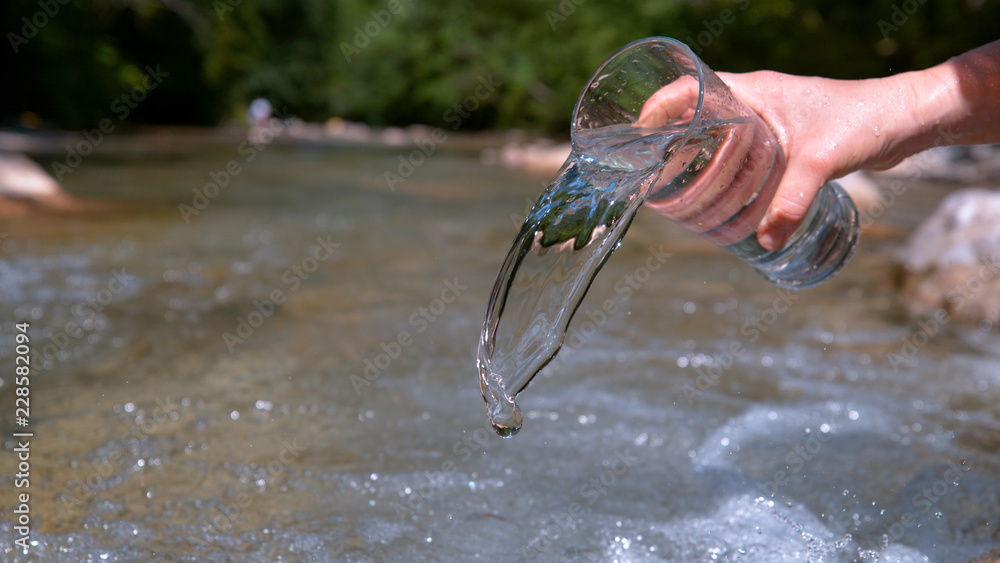 CLOSE UP: Unrecognizable woman pours water back into the river on sunny day.