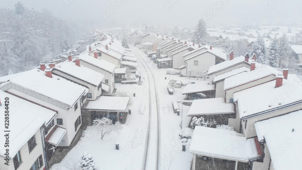 AERIAL: Unrecognizable adult person shoveling their driveway during a snowstorm.