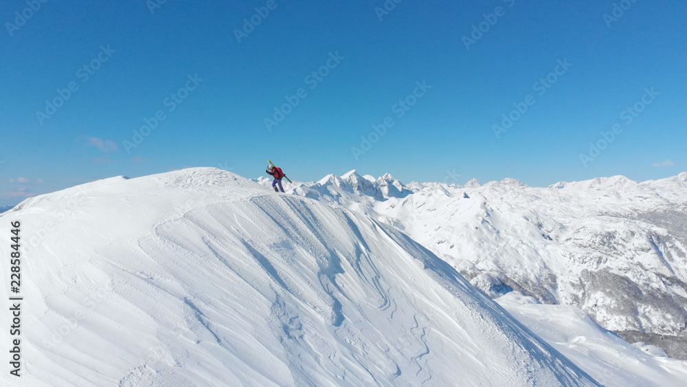 AERIAL: Flying along the snowy mountain ridge being scaled by an unknown skier.